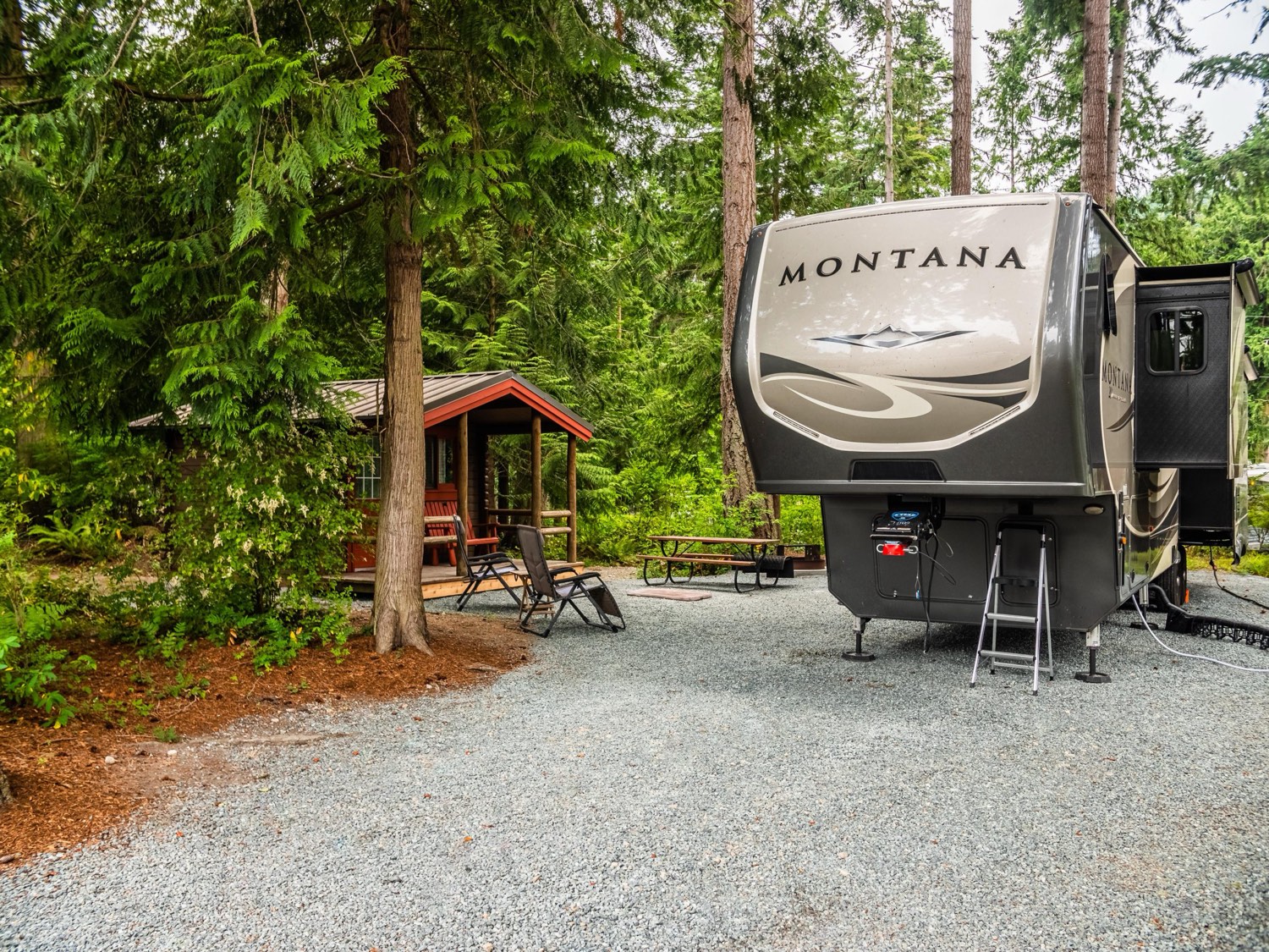 An RV parked on a full-hookup site beside a cabin at Pioneer Trails